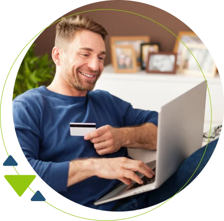 Homem loiro sorrindo, usando blusa azul segurando um cartão e o notebook para utilizar o emissor gratuito de NFe.